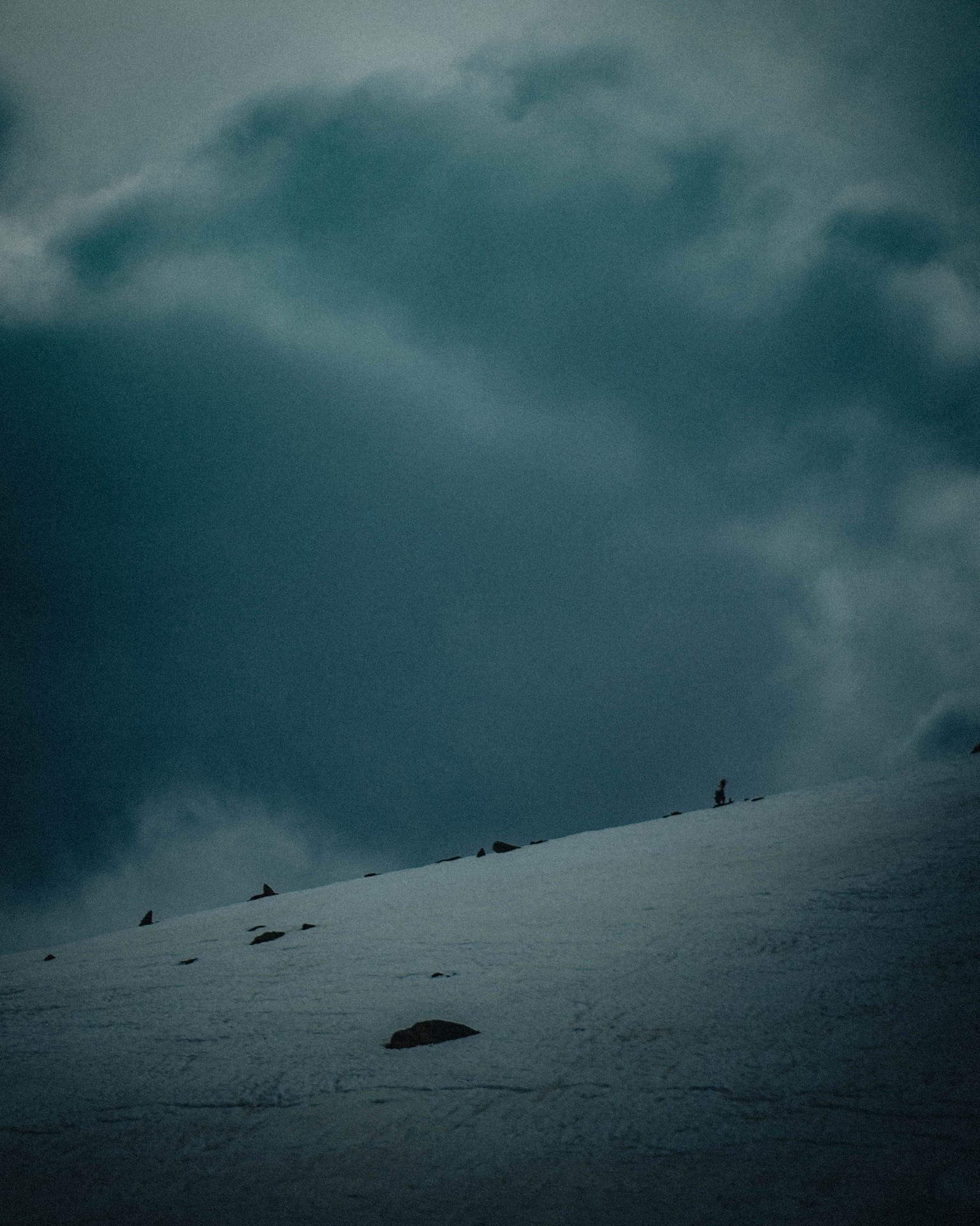 Lone figure on a snowy ridge under brooding storm clouds